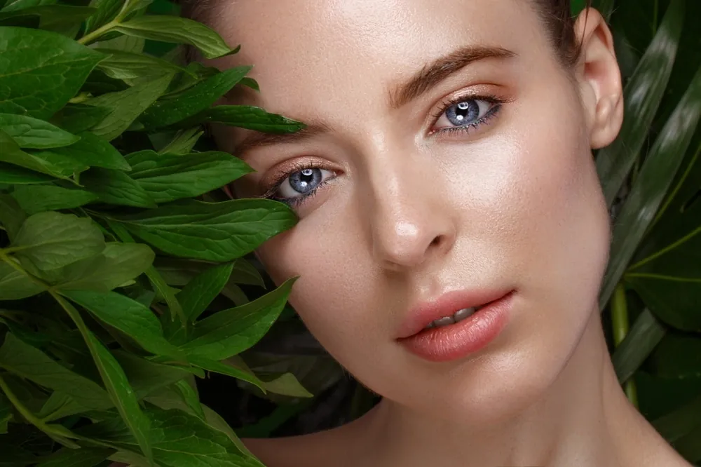 A woman with clear skin and blue eyes beside green leaves