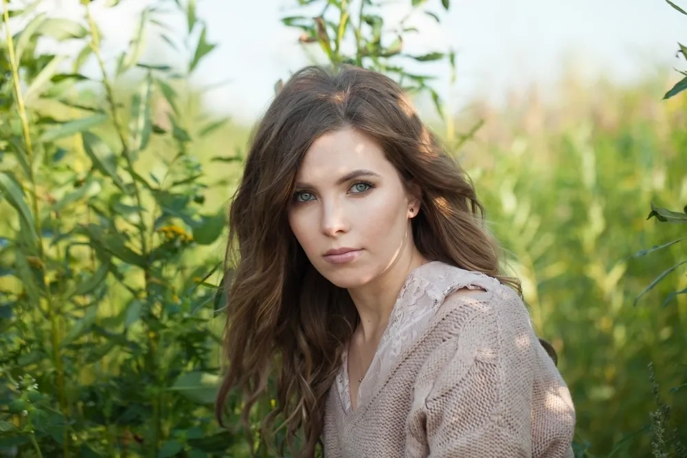 A young woman with wavy brown hair sitting among tall green plants