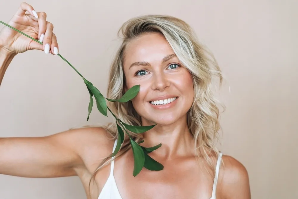 A smiling woman with wavy blonde hair holding a leafy branch