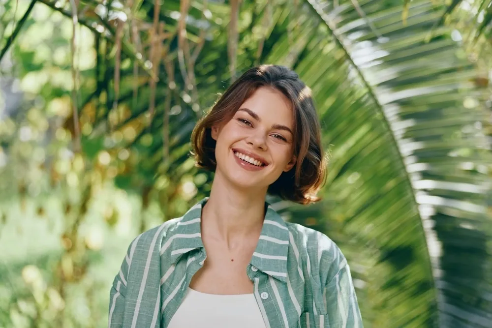 A smiling young woman in a striped shirt in front of palm leaves