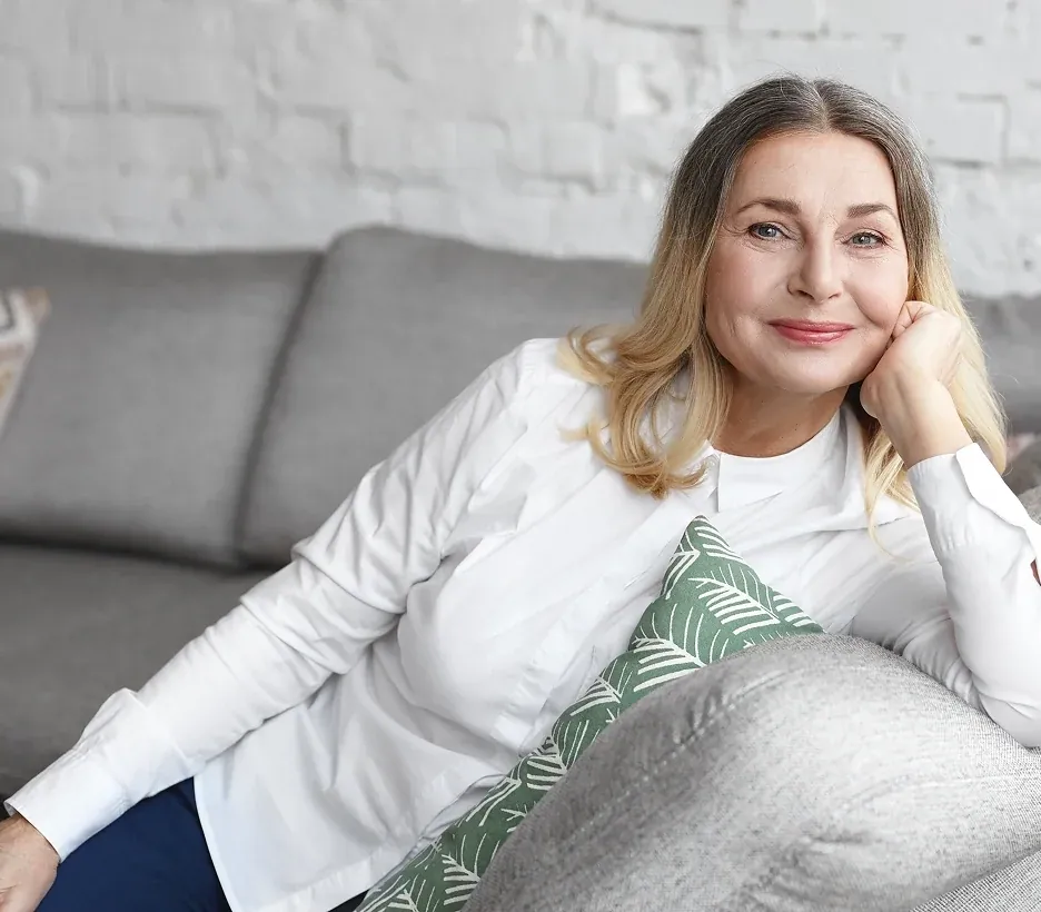 A smiling woman with long blond hair resting her head on her hand on a sofa