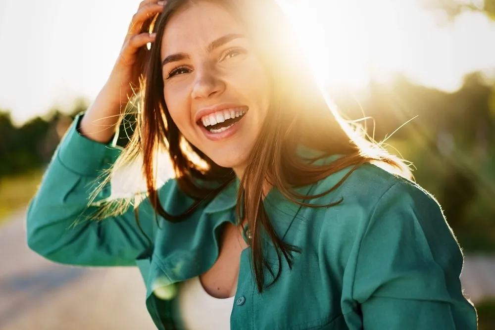 A smiling young woman in a teal shirt standing in sunlight