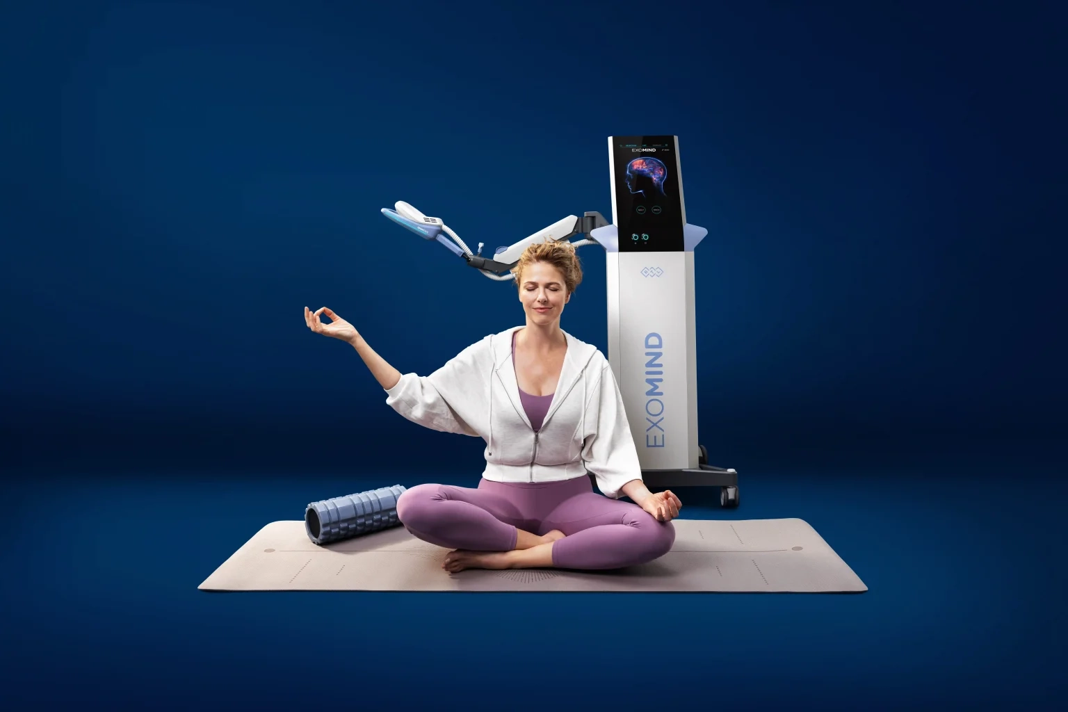 The Exomind device beside a woman seated on a yoga mat