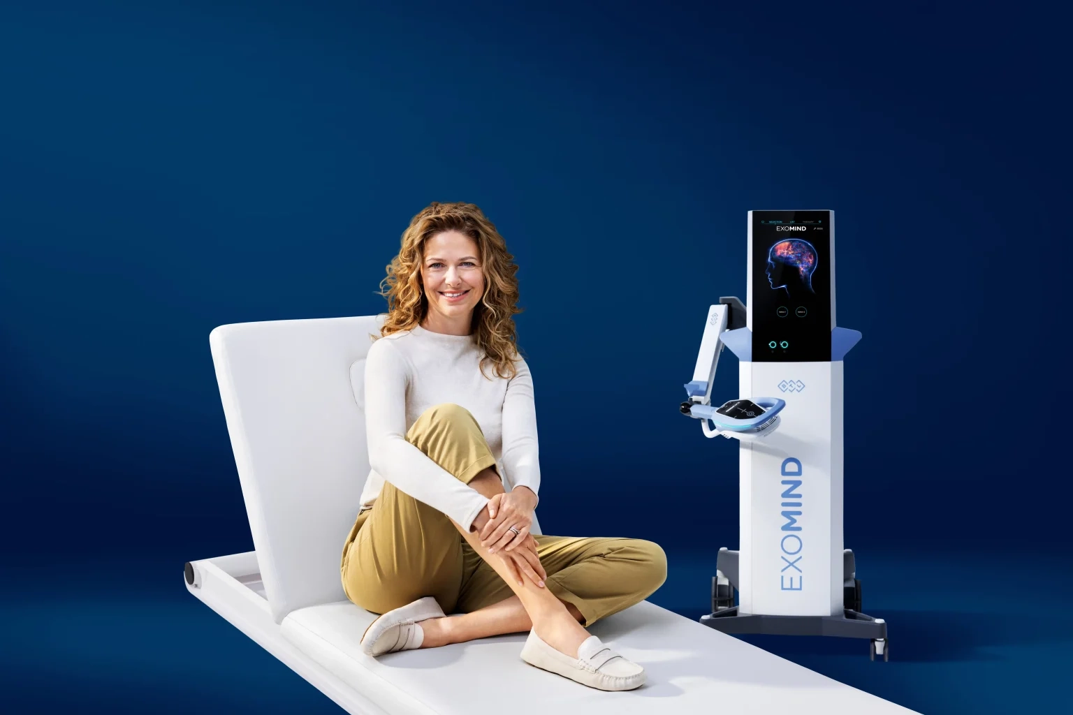 A woman seated on a treatment bed beside the Exomind device