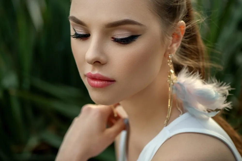 A young woman with a white top looking down, framed by green foliage