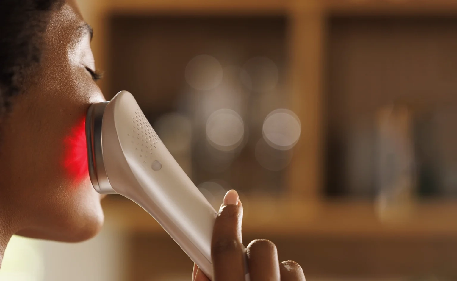 A hand holding a red light device against the cheek