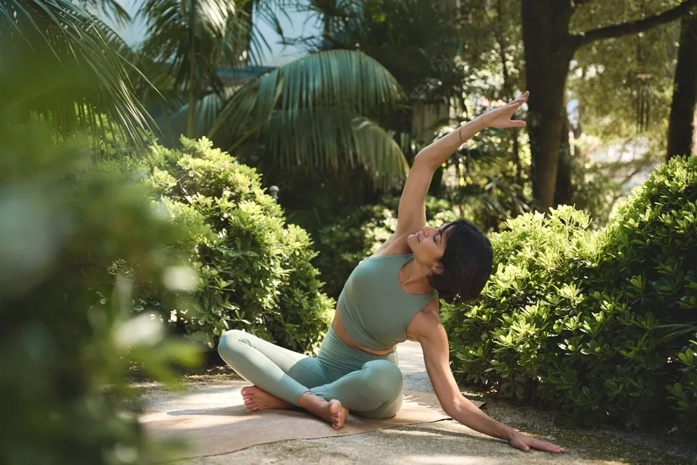 A woman in green activewear doing a seated stretch in a garden