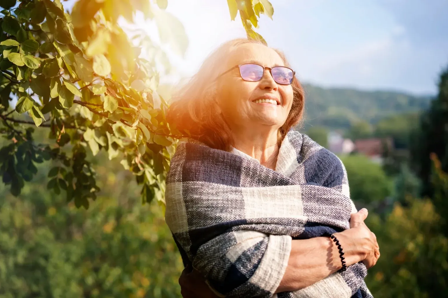 An older woman in sunglasses smiling outdoors in the sun