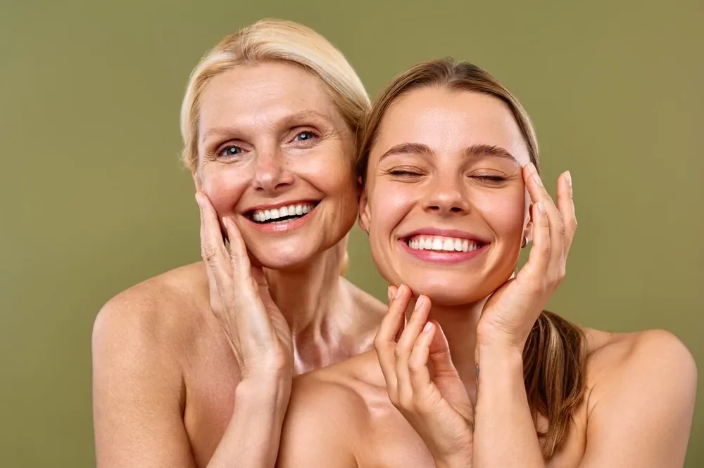Two women of different ages smiling and touching their faces