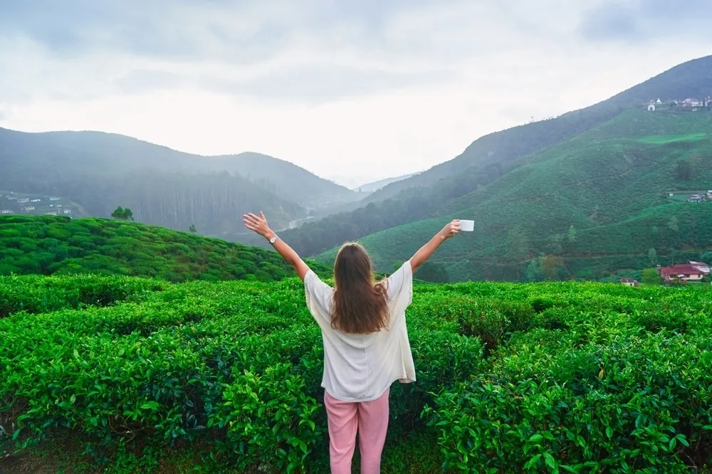 A woman with arms raised standing in green hillside fields