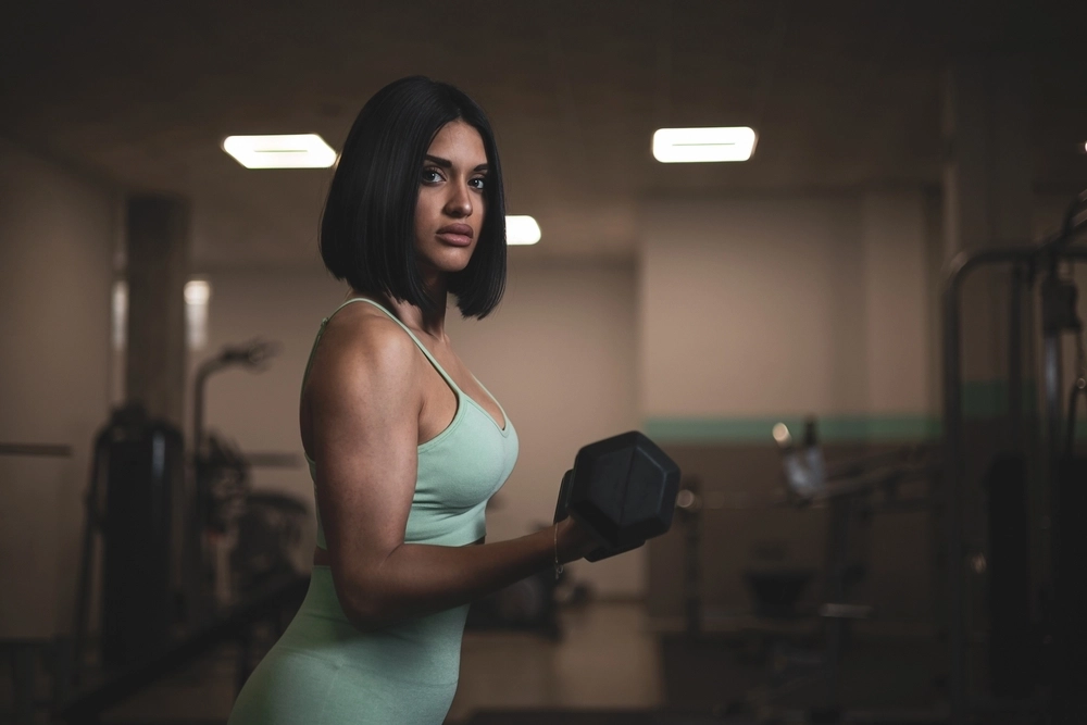 A woman in a green tank top lifting a dumbbell in a gym