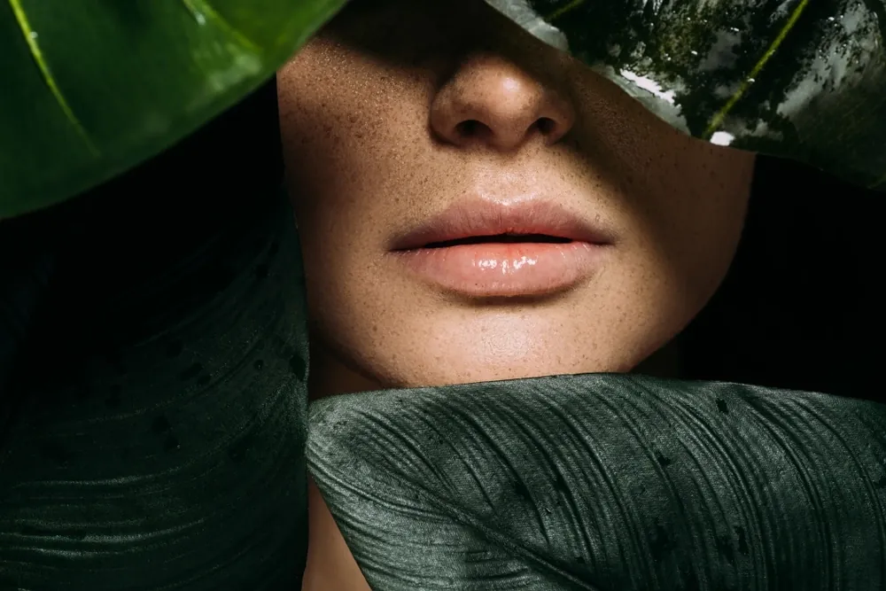 Lips and lower face framed by large green tropical leaves